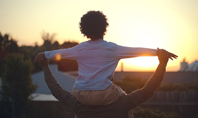 Parent holding their child on their shoulders, enjoying the sunset